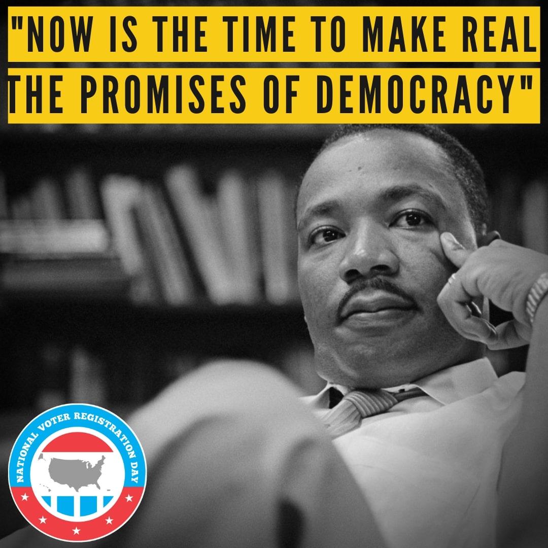 Black and white photo of Martin Luther King, Jr. with books behind him. Text reads: Now is the time to make real the promises of democracy."